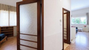 A room with a wooden door, a bed, a bedside table, a nightstand, a window, and a view of a garden. - Casa Carletti - Le Ghiaie (Portoferraio)