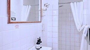 Casa de banho com lavatório branco, espelho, chuveiro e barra para toalhas.