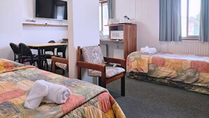 Quarto de hotel com duas camas, uma escrivaninha, uma cadeira, uma televisão e uma janela com cortinas.