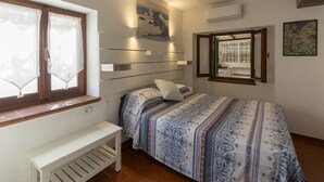 Ein Schlafzimmer mit Bett, Sitzbank, Fenster mit Vorhängen, Wandklimaanlage und einem Gemälde.