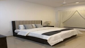 Quarto moderno com uma cama grande, mesa de cabeceira, ventilador de teto e janela com cortinas.