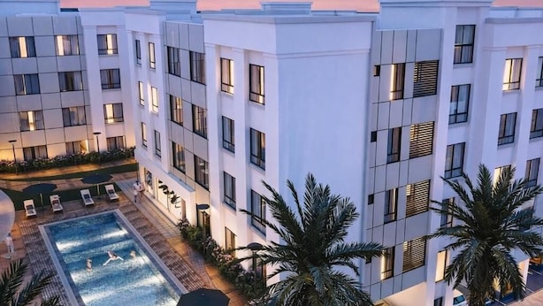 Um hotel moderno com piscina no terraço, várias varandas e palmeiras.