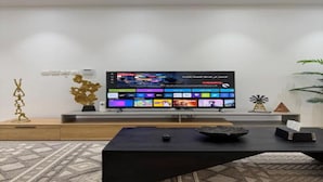 Uma sala de estar moderna com uma TV de tela plana na parede, uma mesa de centro preta e objetos decorativos.