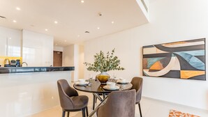 A modern dining area with a round table, four chairs, and a vase with greenery. - Contemporary 2BR, Mins. Drive to Butterfly Garden (Dubai)