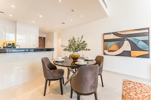 A modern dining area with a round table, four chairs, and a vase with greenery. - Contemporary 2BR, Mins. Drive to Butterfly Garden (Dubai)