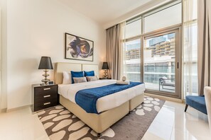 A modern bedroom with a large bed, two bedside tables, a window with a city view, and a decorative rug. - Contemporary 2BR, Mins. Drive to Butterfly Garden (Dubai)