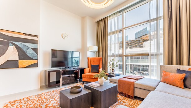 A modern living room with a large window, a flat-screen TV, a sofa, and a coffee table. - Contemporary 2BR, Mins. Drive to Butterfly Garden (Dubai)