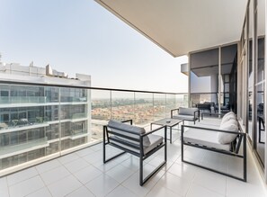 A modern balcony with a glass railing, a sofa, a coffee table, and a view of a cityscape. - Contemporary 2BR, Mins. Drive to Butterfly Garden (Dubai)