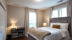 Une chambre à coucher avec un lit, un bureau, une chaise et une fenêtre avec des rideaux.