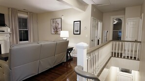 Un salon comprenant un canapé, une cheminée, un escalier et une porte donnant sur une autre pièce.