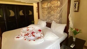A neatly made bed with a canopy, a bedside table with a vase of flowers, and a wall with a decorative pattern. - 2 Livu Villas Watamu (Watamu)
