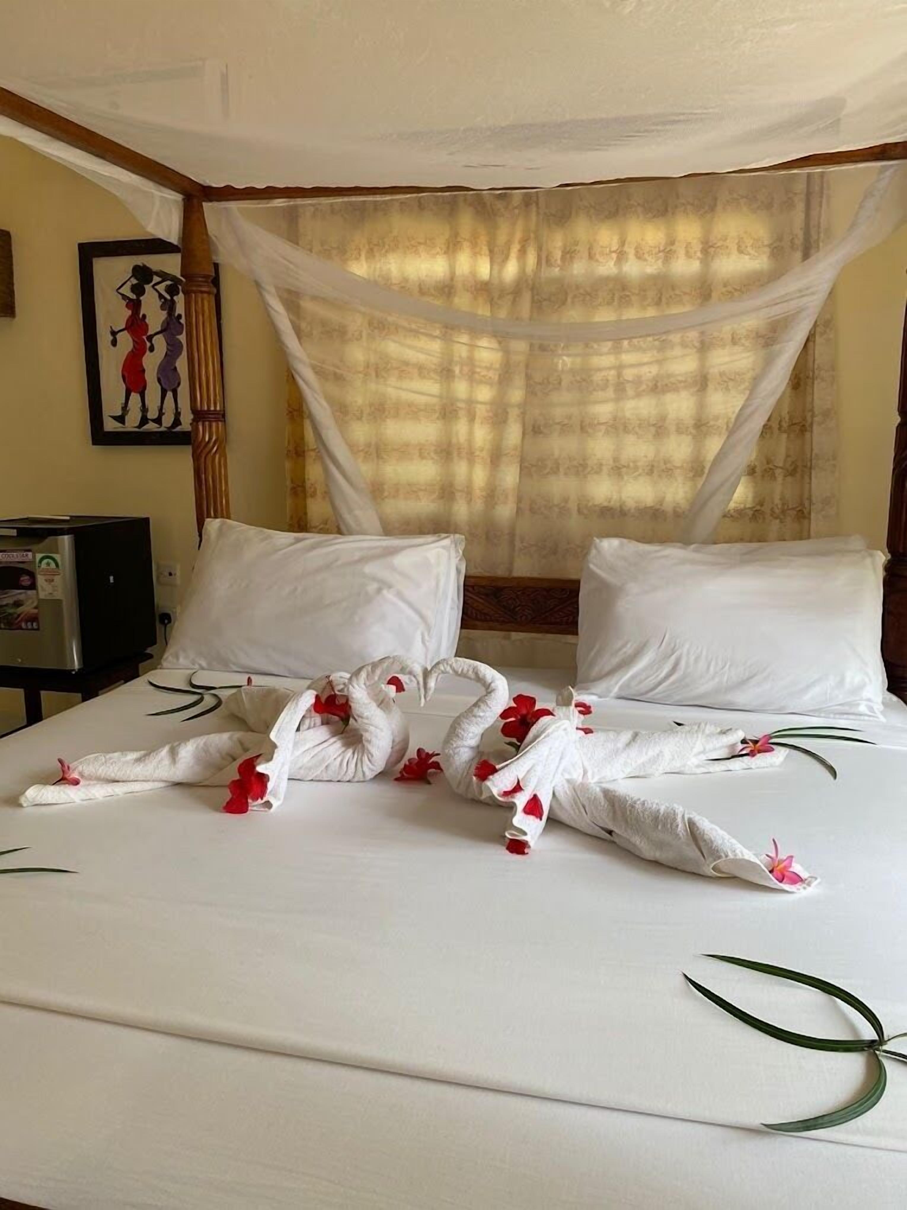 Una habitación de hotel con una cama, almohadas blancas, dosel y un cuadro en la pared.