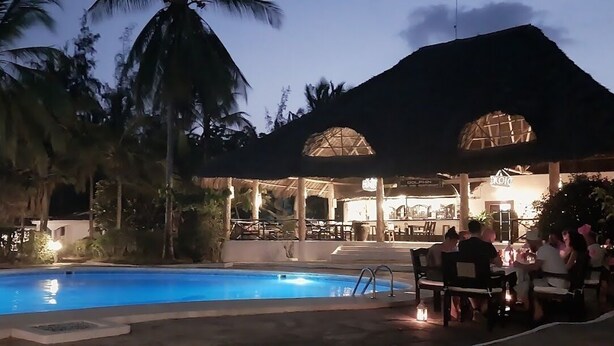 A pool area with a thatched-roof structure, palm trees, and a dining area with tables and chairs. - 2 Livu Villas Watamu (Watamu)