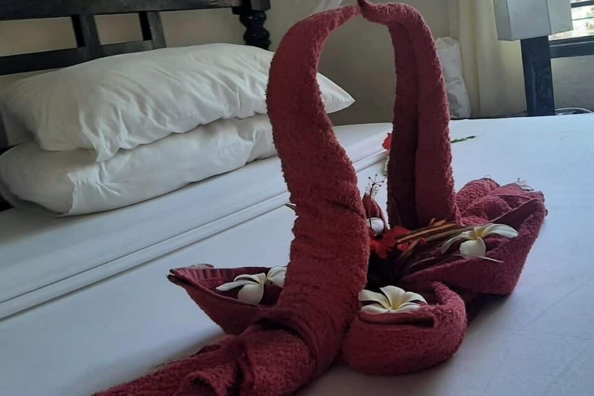 Un lit avec du linge de lit blanc, une tête de lit en bois foncé et une serviette rouge disposée de manière décorative avec des fleurs.