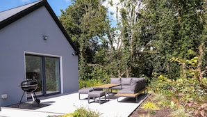Eine moderne Außenpatio mit integriertem Grill, einem grauen Sofa und verschiedenen Pflanzen und Blumen.