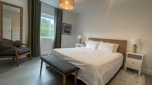 Ein ordentlich eingerichtetes Schlafzimmer mit einem großen Bett, einer Bank, einem Sessel und einem Nachttisch mit Lampe.