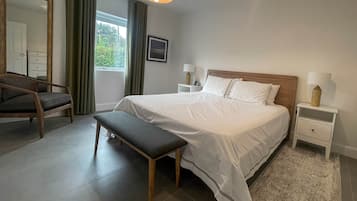 Quarto bem organizado com uma cama grande, um banquinho, uma cadeira e uma mesa de cabeceira com abajur.