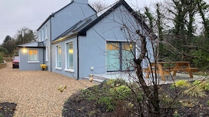 Ein modernes, zweistöckiges Haus mit Kiesweg, Holzbank und einem kleinen Garten.