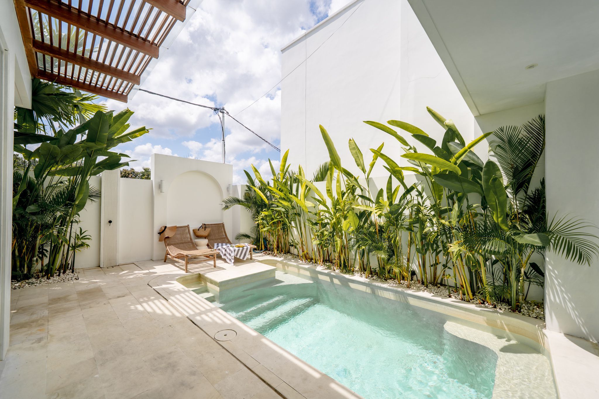 Una piscina con sillones de descanso y plantas tropicales.