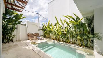 Una piscina con sillones de descanso y plantas tropicales.