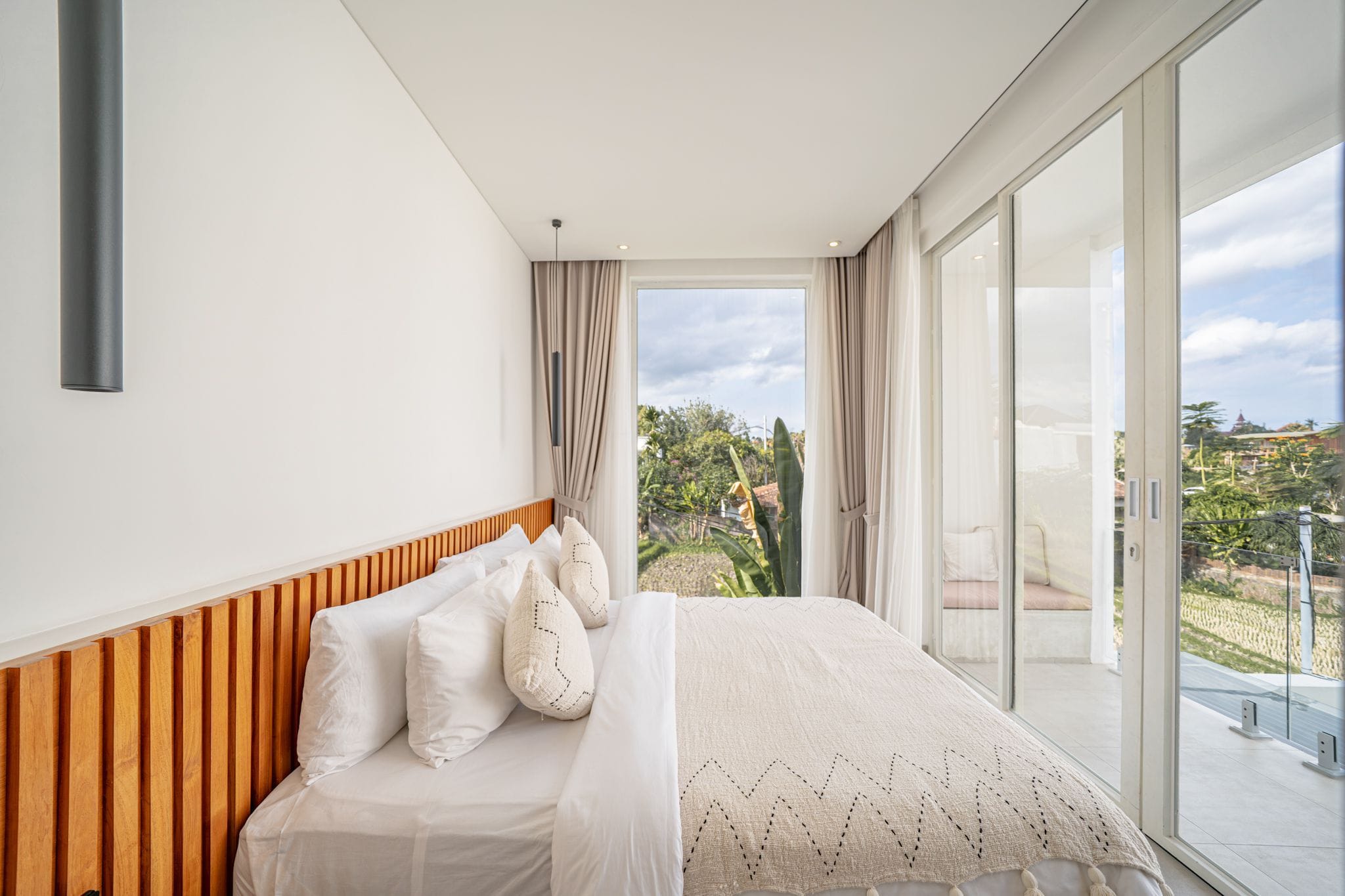 Un dormitorio con una cama grande, cabecera de madera y vistas a un jardín a través de una puerta corrediza de vidrio.