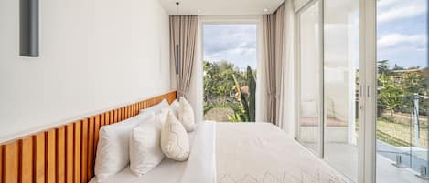 Un dormitorio con una cama grande, cabecera de madera y vistas a un jardín a través de una puerta corrediza de vidrio.
