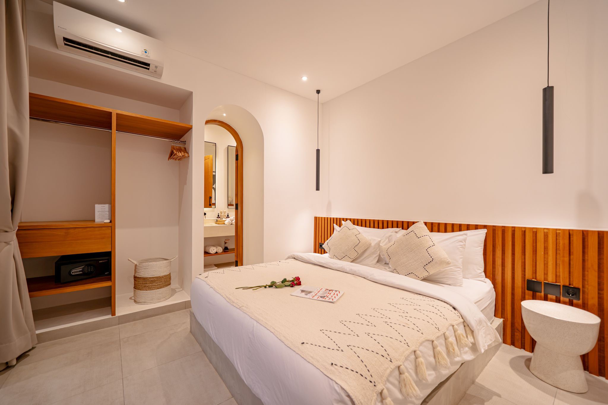 A modern bedroom with a large bed, a wooden headboard, a bedside table, a white toilet, and a walk-in closet with a mirror.