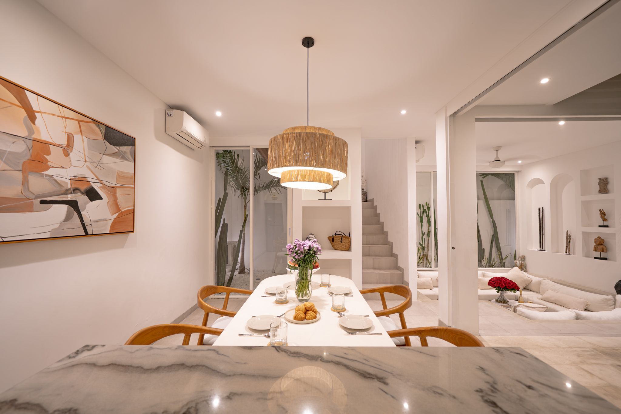 Un comedor moderno con una mesa de mármol, sillas de madera y una lámpara colgante.
