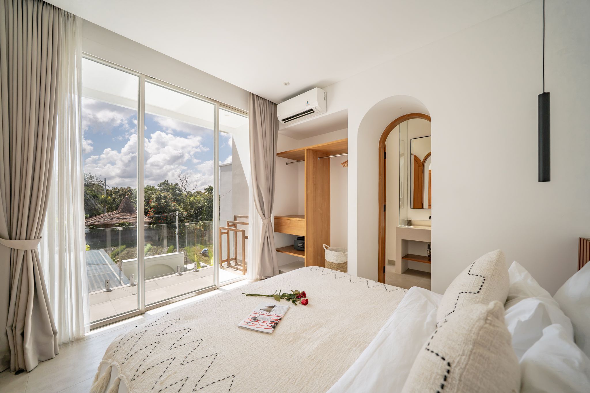 Un dormitorio con un ventanal grande, una cama, un armario y un baño visible a través de un arco.