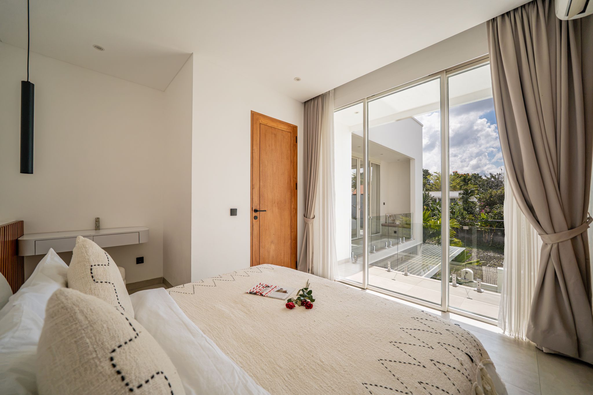 Un dormitorio moderno con una cama grande, una mesita de noche, un armario y un ventanal corredero que da a un balcón.