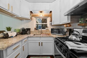 A compact kitchen with white cabinets, a stainless steel stove, a microwave, and a coffee maker. - The cabin is located close to many of Big Bear's most popular attractions (Big Bear)