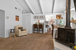 A living room with a fireplace, a sofa, and a kitchen in the background. - The cabin is located close to many of Big Bear's most popular attractions (Big Bear)