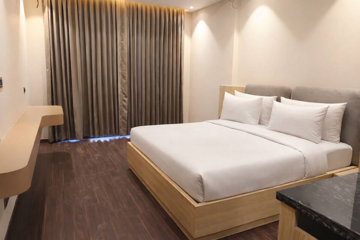 A modern hotel room with a wooden bed frame, a wooden desk, and a dark wooden floor.