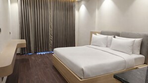 Moderni hotellihuone, jossa on suuri sänky, puinen alusta ja työpöytä tuolilla.