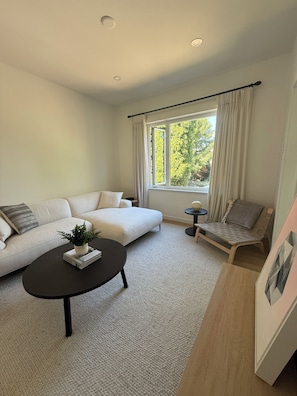 Ein modernes Wohnzimmer mit einer Couch, einem Couchtisch, einem Beistelltisch und einem Fenster mit Vorhängen.