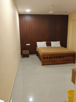 A bedroom with a wooden bed, a nightstand, and a ceiling fan. - JR Residency by k hotel (Tiruvannamalai)