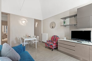 A modern living room with a sofa, a dining table with chairs, a colorful armchair, a flat-screen TV, and built-in cabinets. - Garibaldi (Loano)