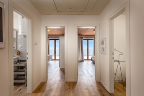 Un couloir mène à deux chambres dotées de planchers en bois, d’un ventilateur de plafond et offrant une vue sur la mer.