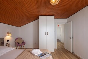 A bedroom with a sloped ceiling, a bed, a wardrobe, a chair, and a reading area with a magazine. - Panoramic Holiday Home Kvarner: Pool & Sea View (Opatija)