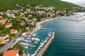 An aerial view of a coastal town with a marina, residential buildings, and a road leading to the waterfront. - Panoramic Holiday Home Kvarner: Pool & Sea View (Opatija)