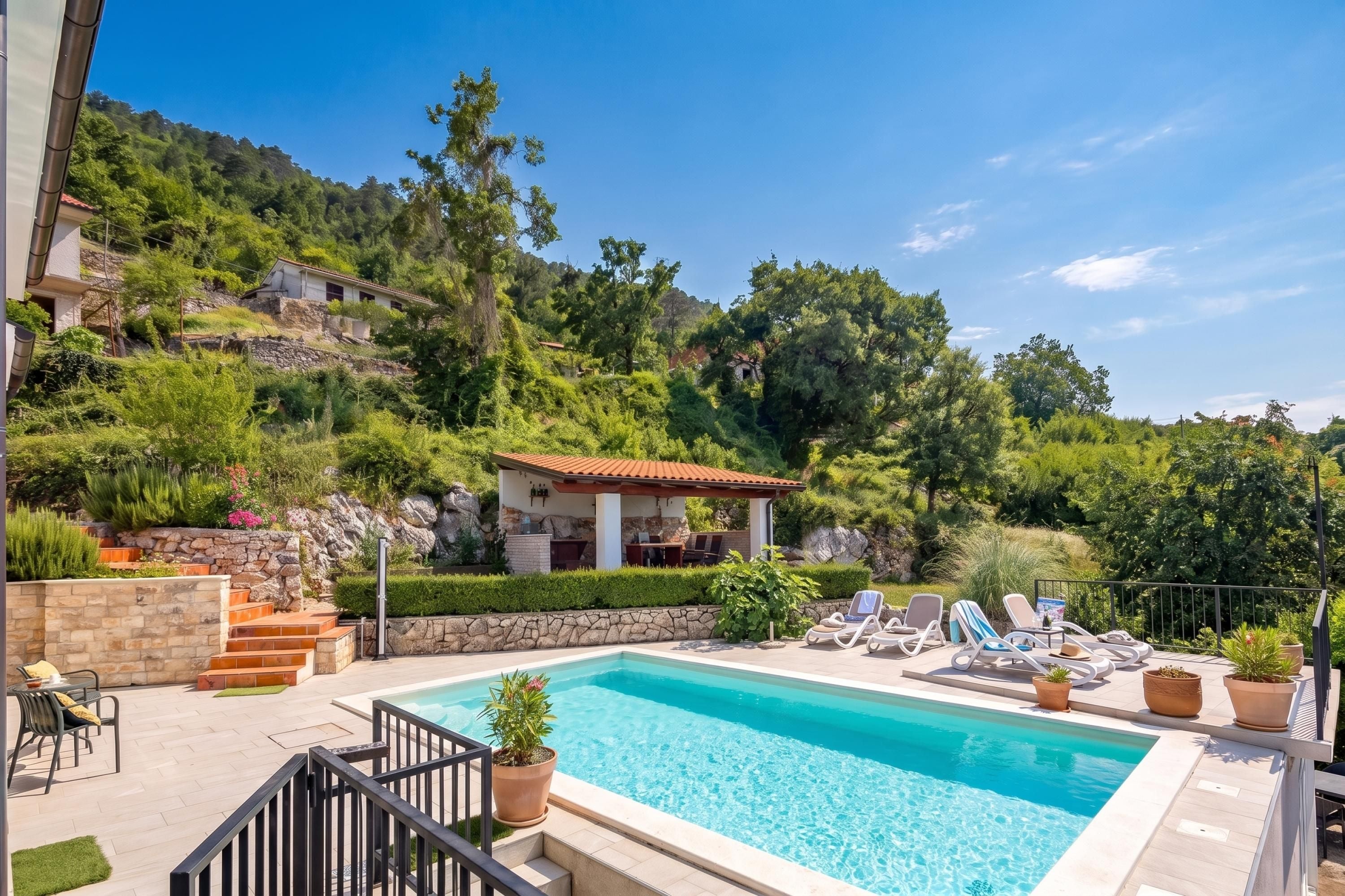 Una piscina con sillones reclinables, una escalera de piedra y vistas a una ladera con edificios.