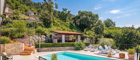 A swimming pool with lounge chairs, a stone staircase, and a view of a hillside with buildings.