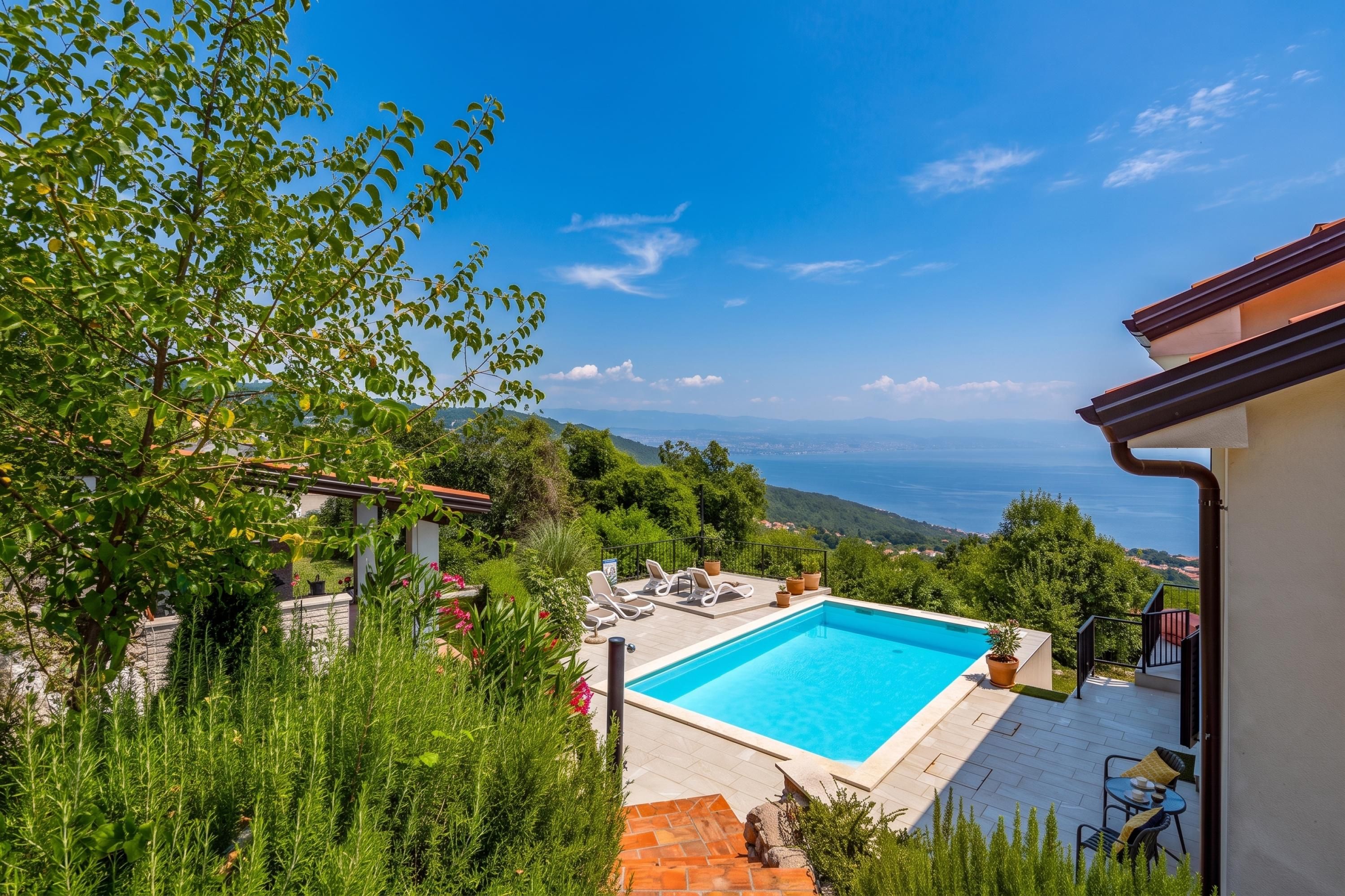 A swimming pool with a view of the sea, surrounded by greenery and a clear sky.