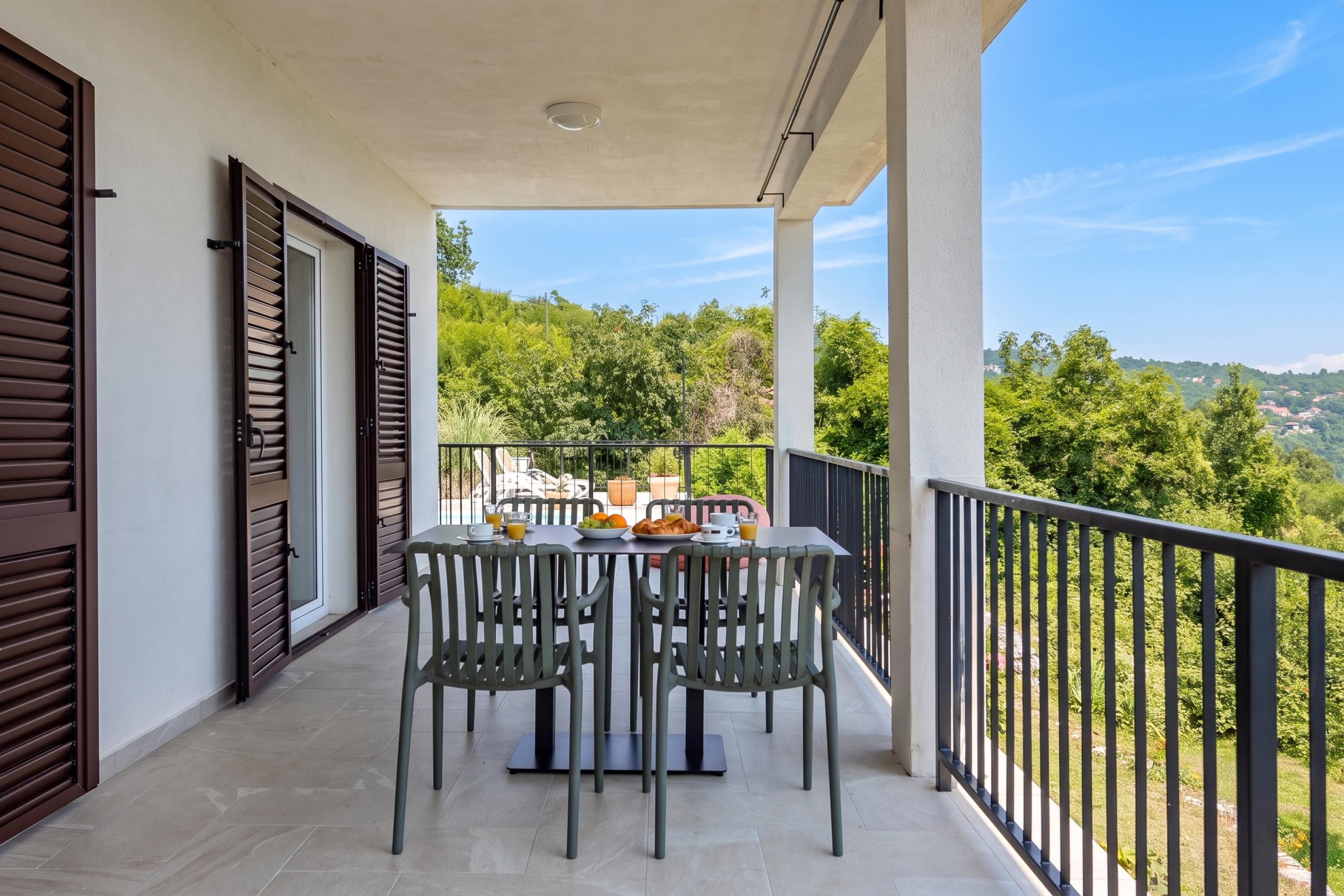 A balcony with a table set for breakfast, overlooking a lush green landscape.