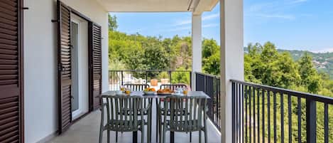 A balcony with a table set for breakfast, overlooking a lush green landscape.