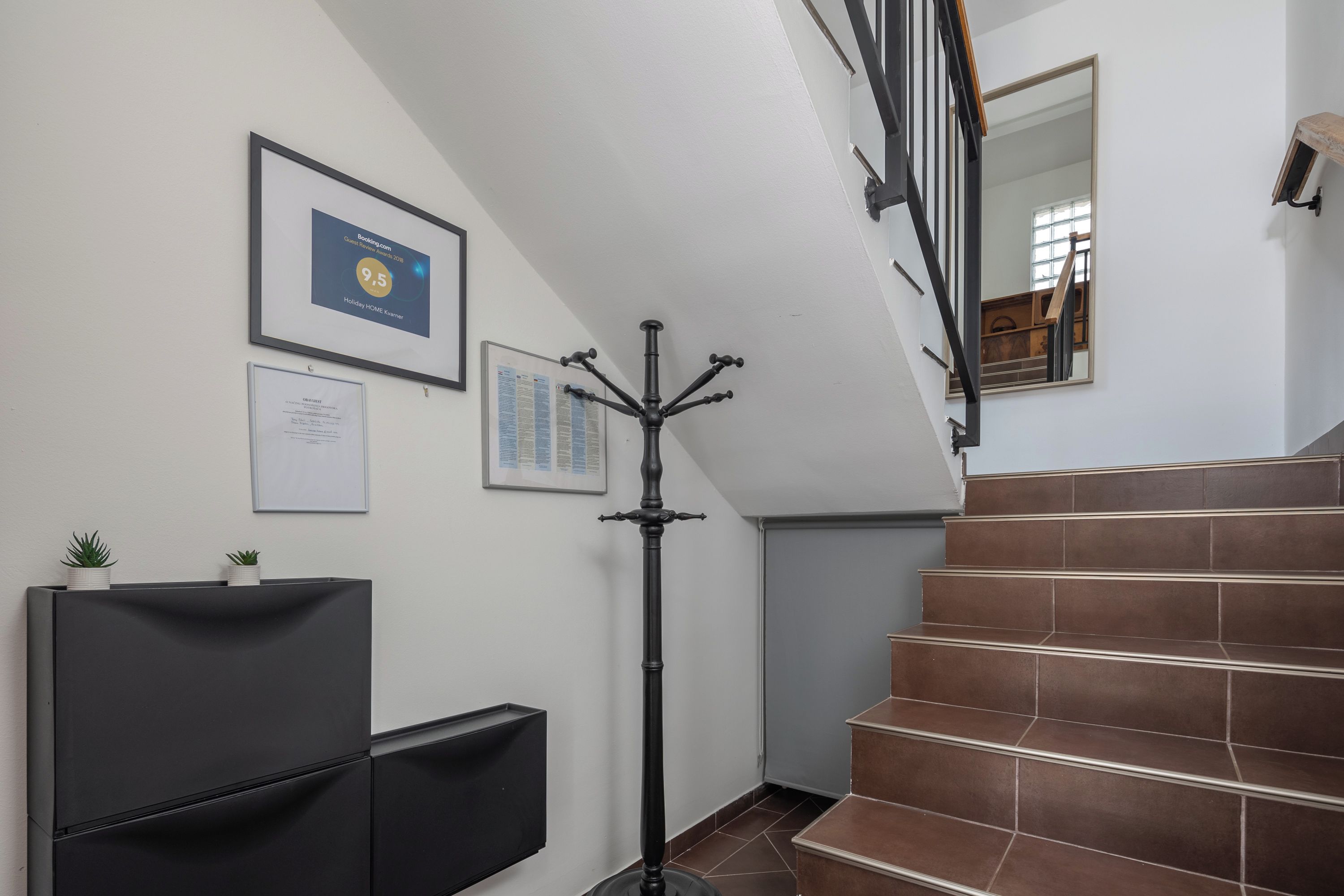 A staircase with brown tiles, a black floor lamp, and framed certificates on the wall.