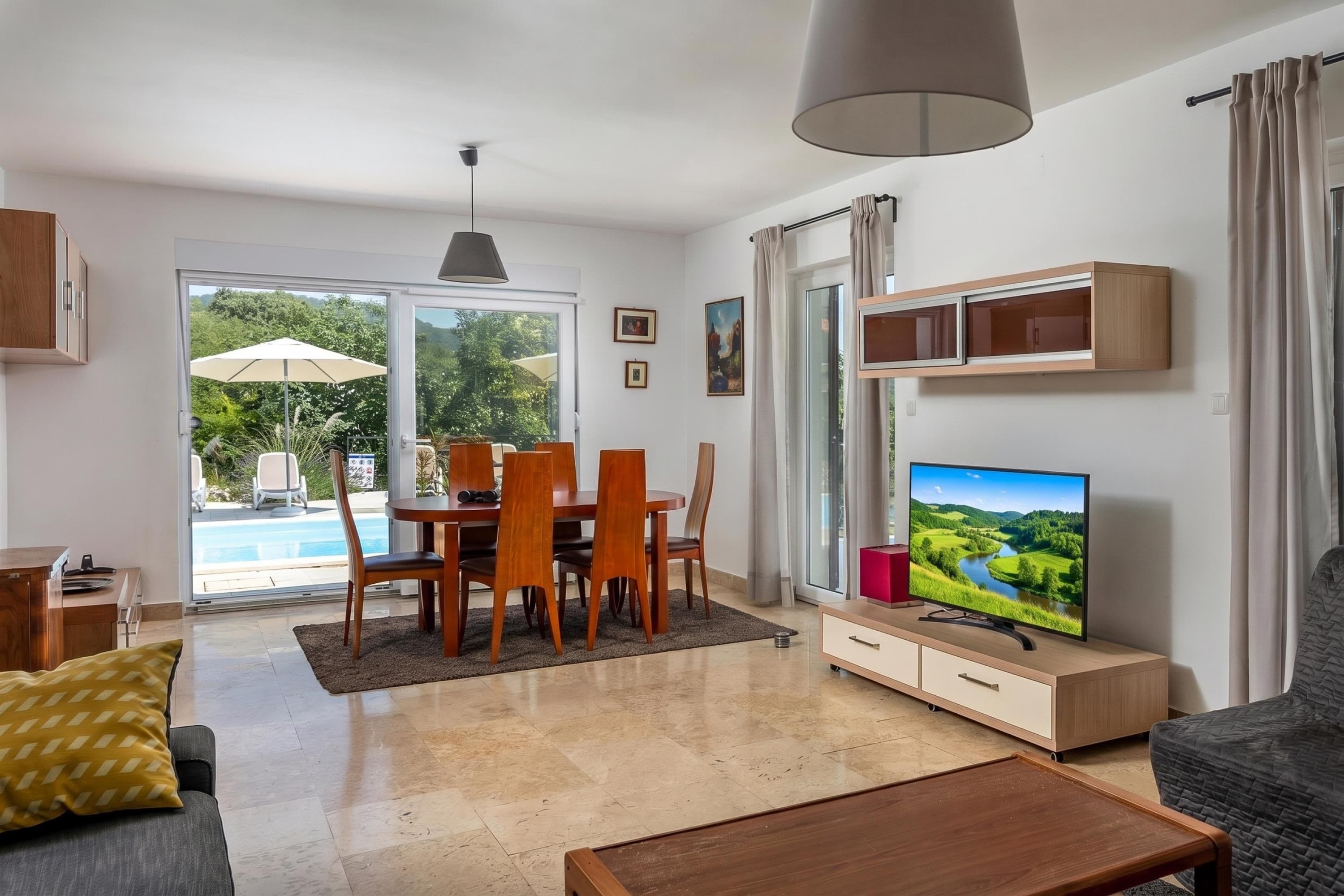 Una sala de estar moderna con comedor, televisor y vista a la piscina.