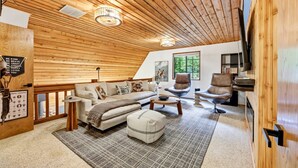 Ein gemütliches Loft-Wohnzimmer mit Holzbalkendecke, einer Sofagarnitur, einem Couchtisch und einem Kamin.
