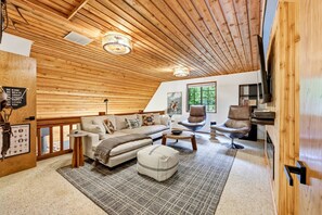 A cozy loft-style living room with a wooden ceiling, a sofa set, a coffee table, and a fireplace. - Forest Hideaway with Hot Tub, Custom Fire-Pit, BBQ Deck & Cozy Mountain Vibes, Minutes to Mountain (Mount Hood Village)