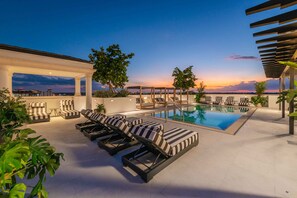Zona de piscina en la azotea con sillones de descanso, piscina y vista del horizonte urbano al atardecer.